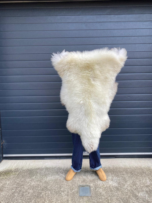 sheepskin rug being held up to show natural markings, mixed cream and beige