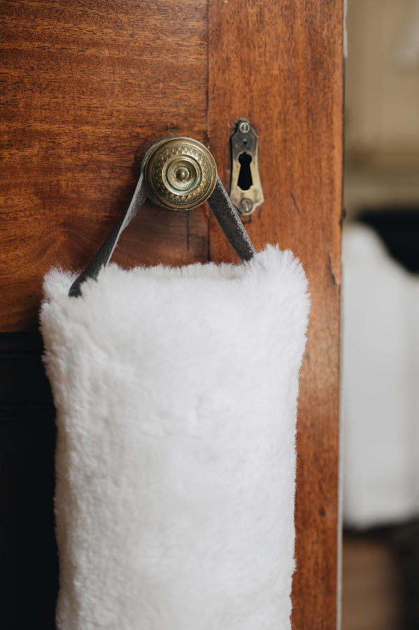 White sheepskin draught excluder with leather handle hanging on a wooden door with a brass doorknob and keyhole.