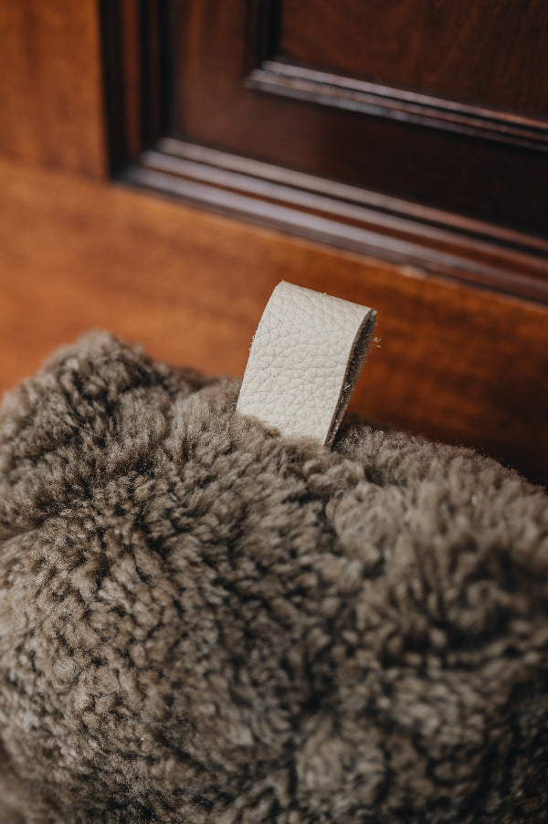 Close up of an oatmeal door stop with leather tabs, holding a wooden door open, on a wooden floor