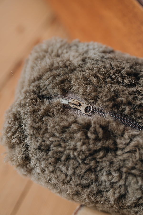 Close-up of the bottom of a brown sheepskin door stop with a zipper on a wooden surface