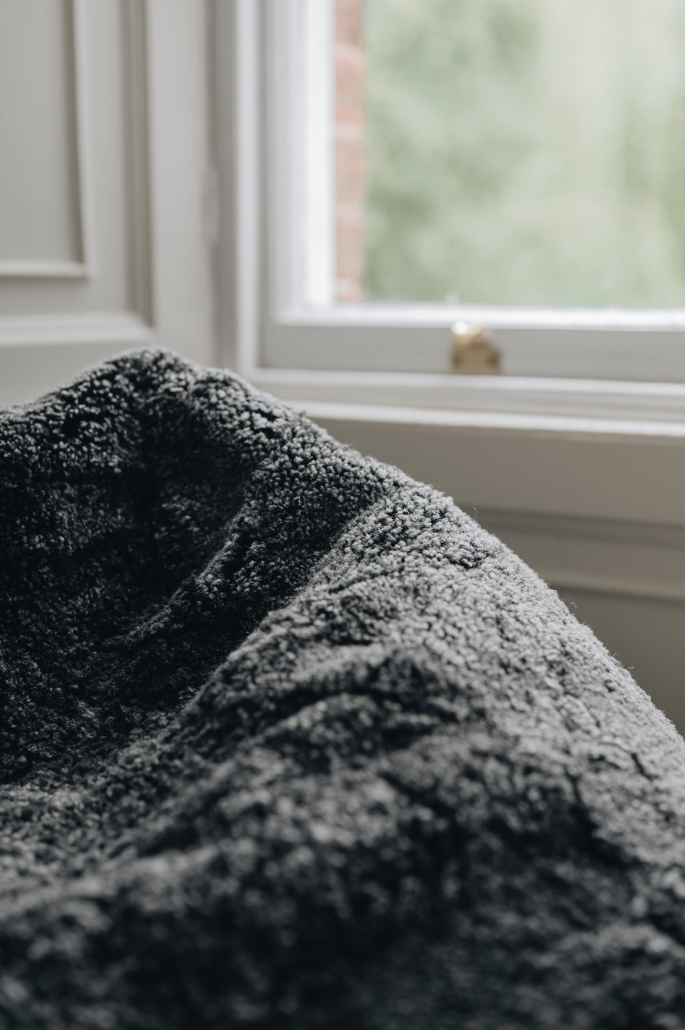 Close-up of a black smoke coloured sheepskin beanbag with a blurred window background.