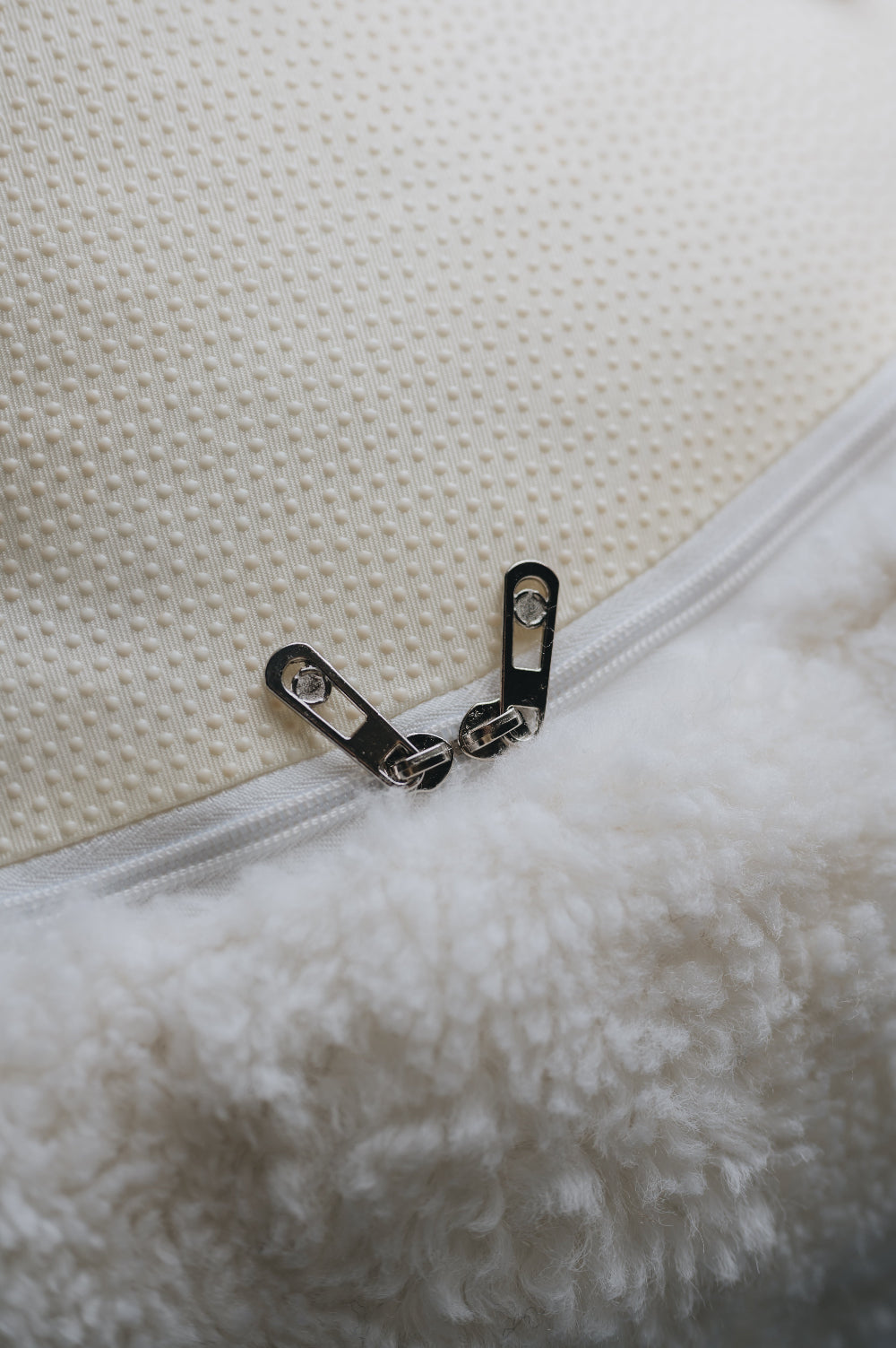 Close-up of a zipper on a textured white surface that is the bottom of a sheepskin beanbag.