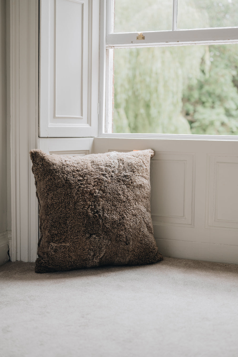 Brown sheepskin textured floor cushion in a window bay with a blurred outdoor view