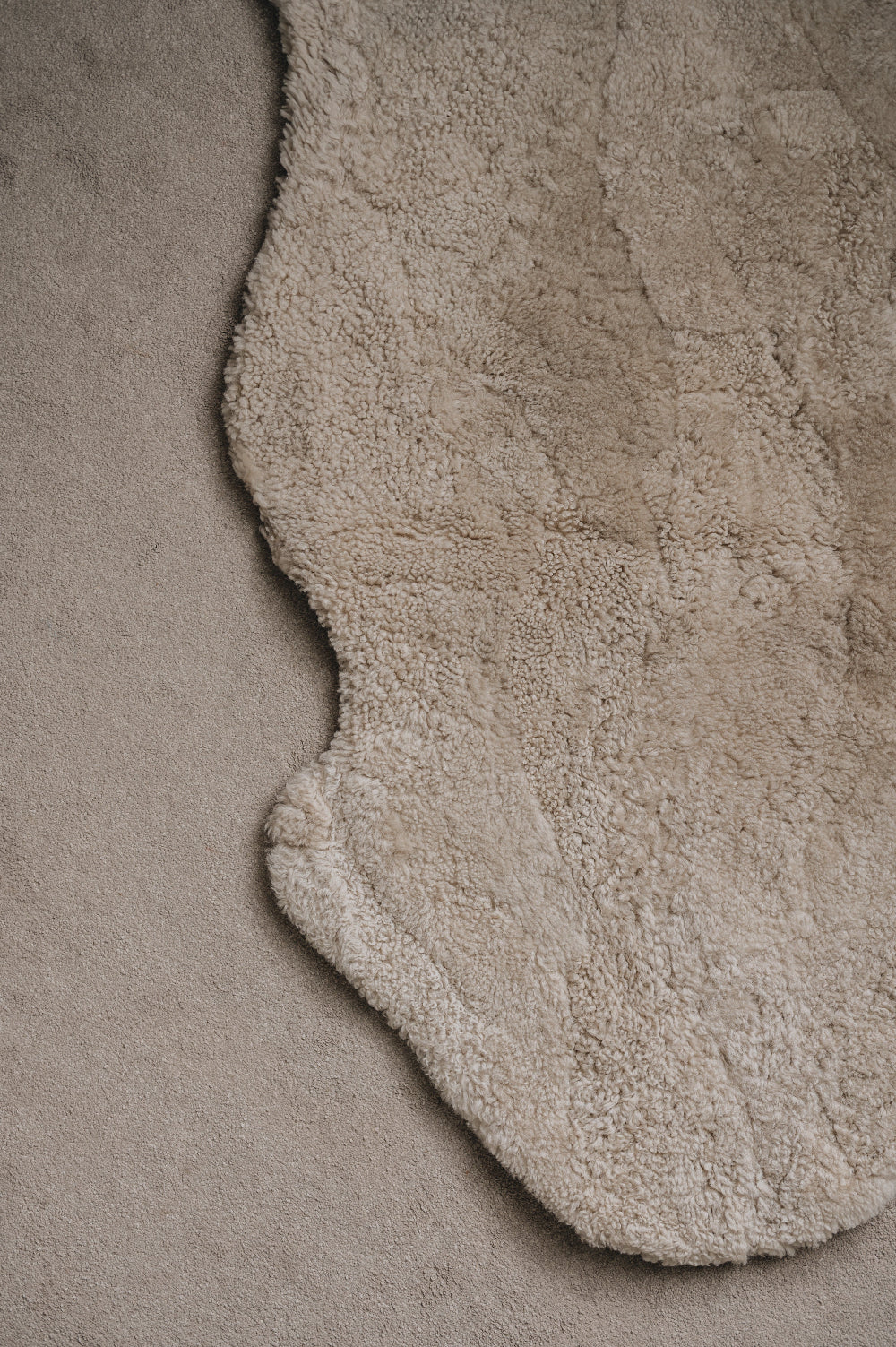 Close-up of an oatmeal sheepskin rug on a similar coloured carpet