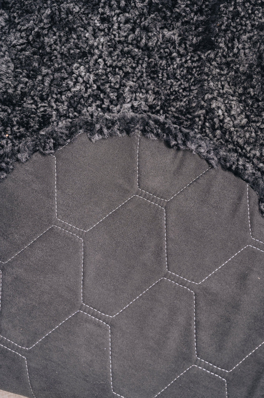 Close-up of a textured dark fabric with a honeycomb pattern on the back / underside of a grey / black sheepskin rug