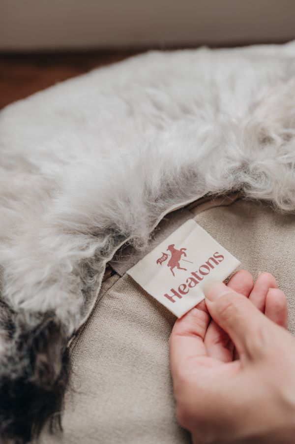 Hand holding a label on a textured fabric surface with 'Heaton's' branding.