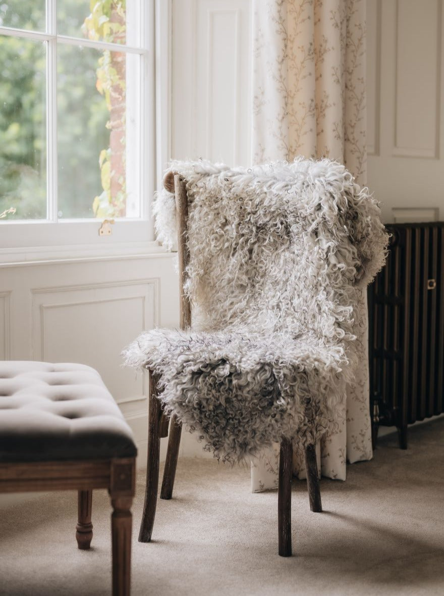 Gotland curly natural grey rug draped over a woodenchair
