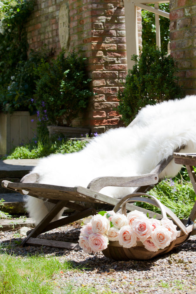 A Dense and plush Natural White British Sheepskin Rug softening up a deckchair in an English Country Garden on a beautiful summers day.
