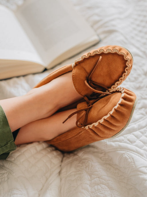 Ava Women's Real Sheepskin Moccasins worn by model with feet up on a bed reading a book 