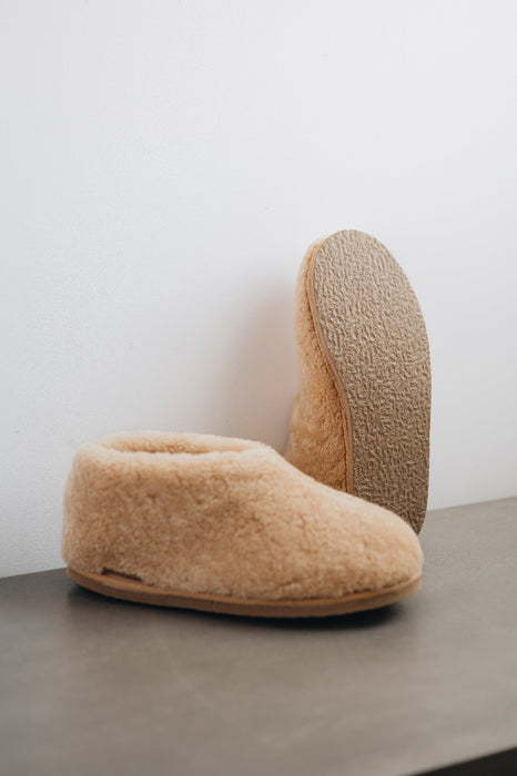 Side and bottom view of a camel coloured curly merino sheepskin boot slipper.