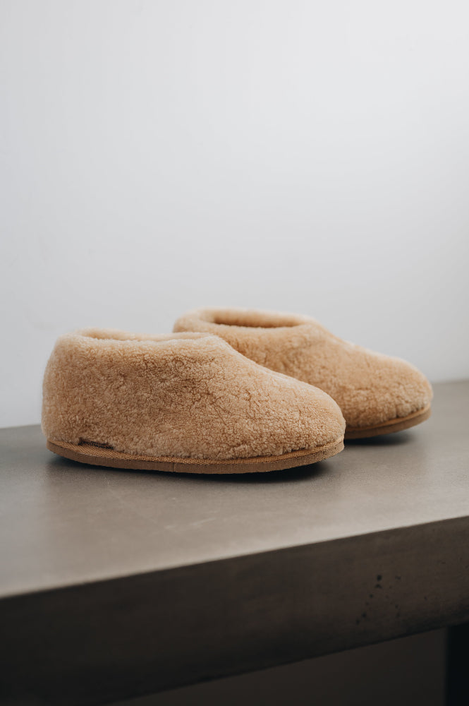 Side view of a camel coloured curly merino sheepskin boot slipper.