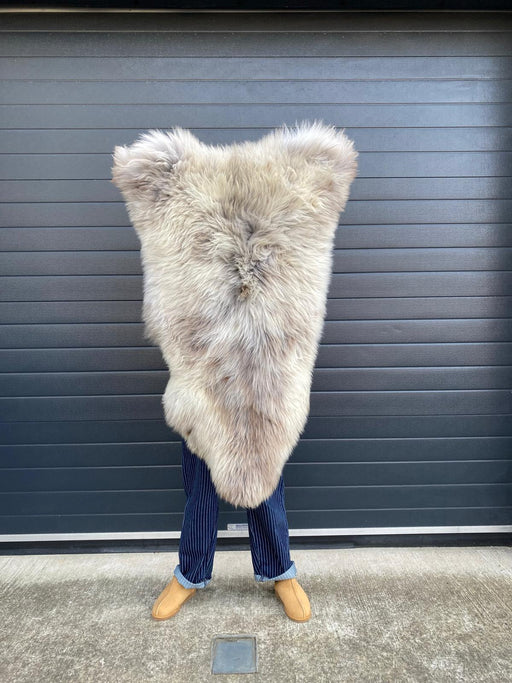 sheepskin rug being held up to show natural markings, an overall cream coloration with a darker brown at the root of the wool