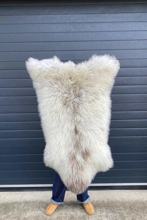 sheepskin rug being held up to show natural markings, cream with very light brown patches down centre of rug