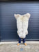 sheepskin rug being held up to show natural markings, cream with light beige  patches and stripe own centre of rug