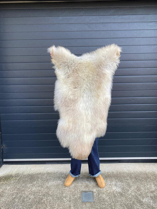 sheepskin rug being held up to show natural colouration, cream and beige mix