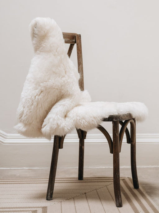 Short Wool Icelandic Sheepskin Rug in white, hung over a wooden chair