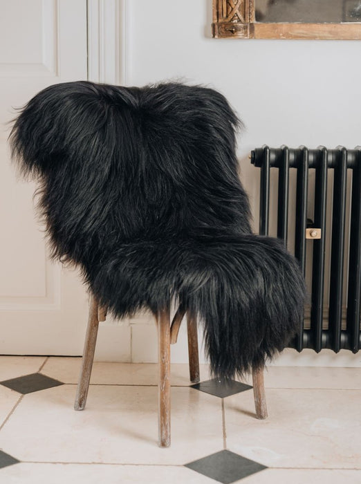 A deep black/brown Icelandic Sheepskin Long Wool Rug. Draped over a brown wooden chair.