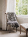 Gotland curly natural grey rug draped over a woodenchair