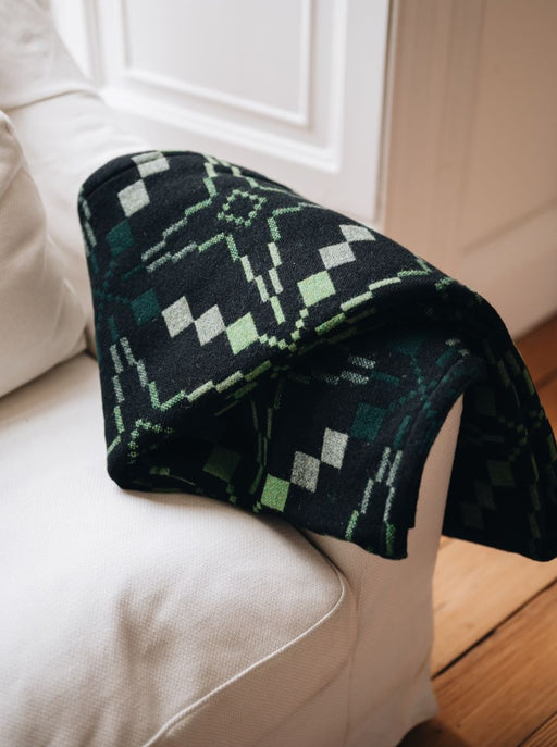 Woodland Green Vintage Star Wool Throw, Melin Tregwynt woven wool throw. Features Vintage Star repeating pattern in deep brown, light and rich greens. Draped over a sofa.