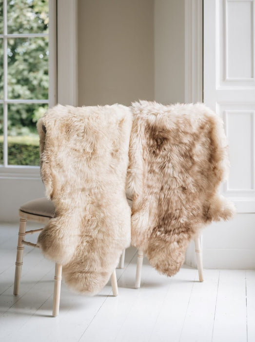 Two Natural melange coloured Swedish Sheepskin Rugs draped over the back of two wooden chairs sitting in a window