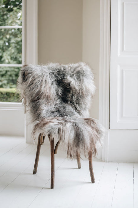 Natural grey undyed Icelandic Sheepskin Rug draped over a wooden chair settled in a window