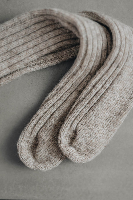 Ribbed beige natural merino wool sock on a light grey background - detail of ribbed sock and toe post