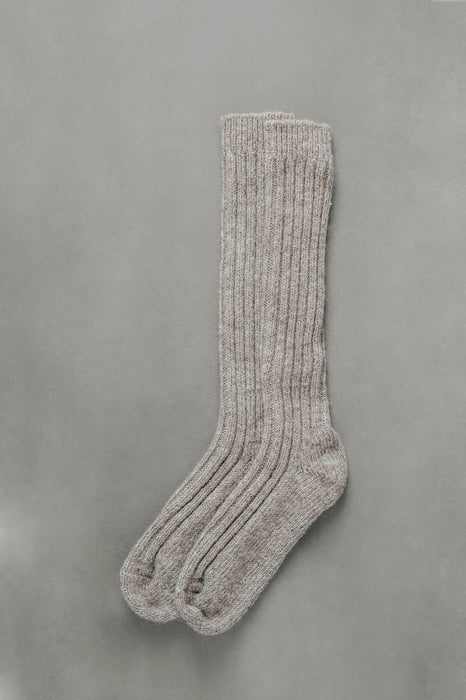 Ribbed beige natural merino wool sock on a light grey background.