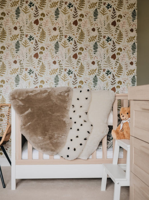 Sheepskin Nursing rugs in Toast, Spotted and Milk draped over a cot in a nursery