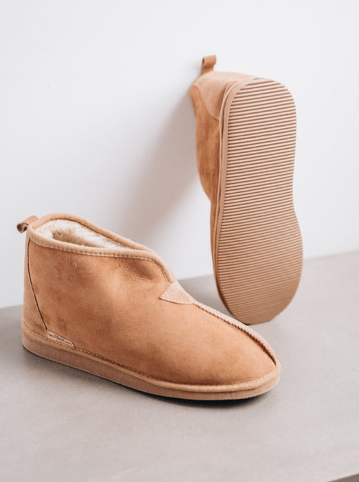 mens sheepskin boot slipper on a grey surface, one slipper balanced against wall to show EVA foam sole