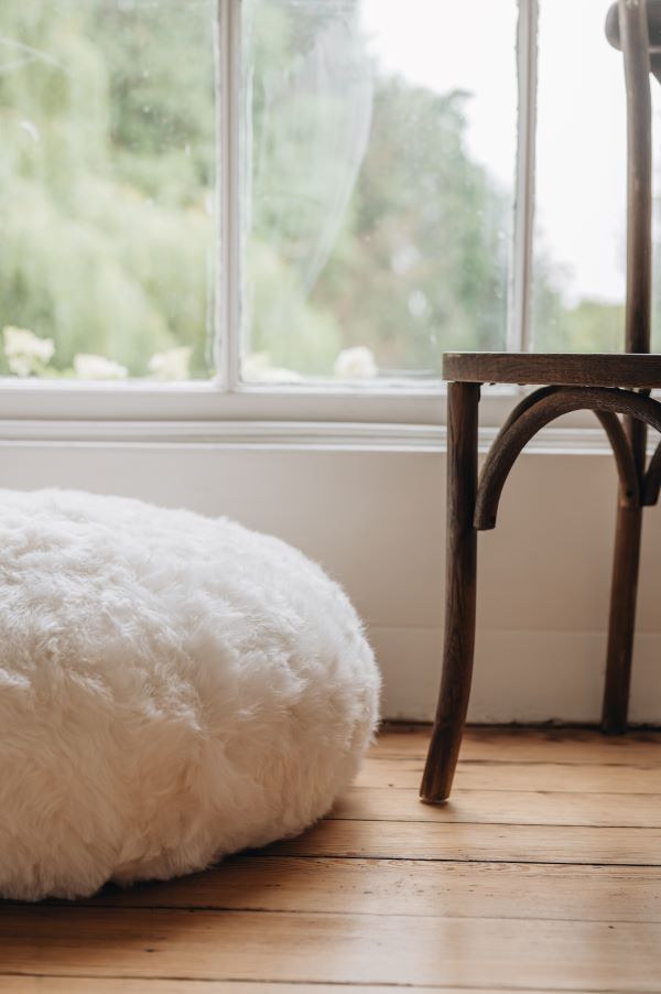 White sheepskin footstool and wooden chair on a wooden floor with a window in the background