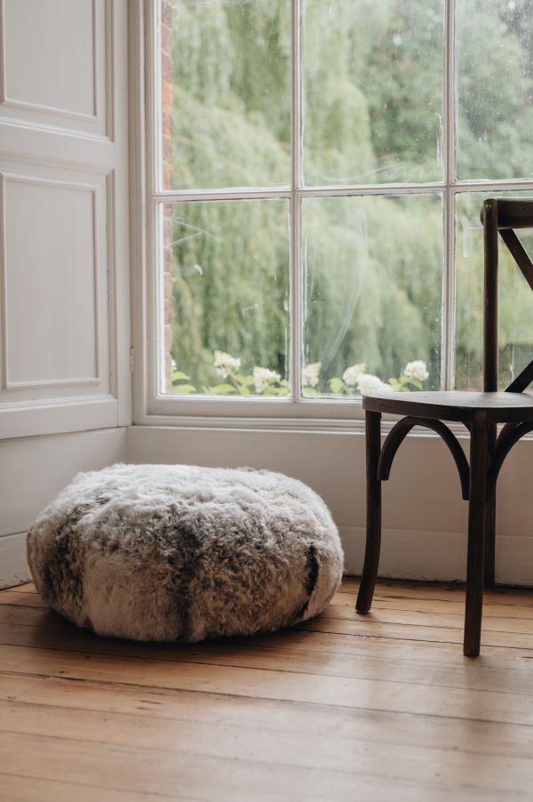 Melange sheepskin ottoman on a wooden floor with a large window in the background