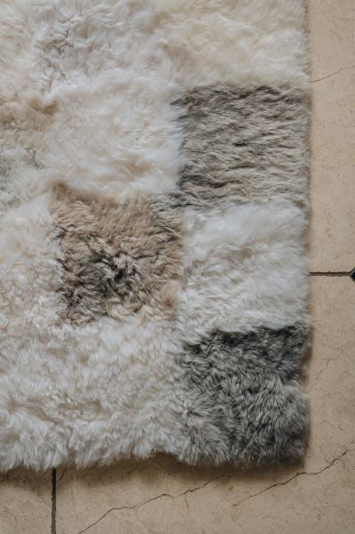 Patchwork rug of sheepskin squares in various natural melange shades on a beige floor.