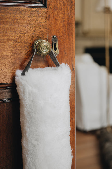 White sheepskin draught excluder with leather handle hanging on a wooden door with a brass doorknob and keyhole.