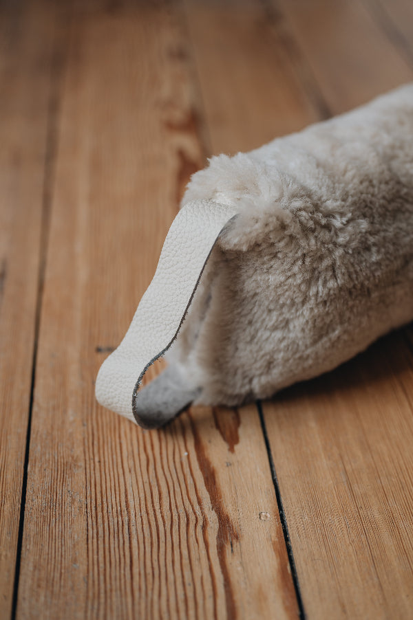 Oatmeal sheepskin draught excluder with light handle on a wooden floor