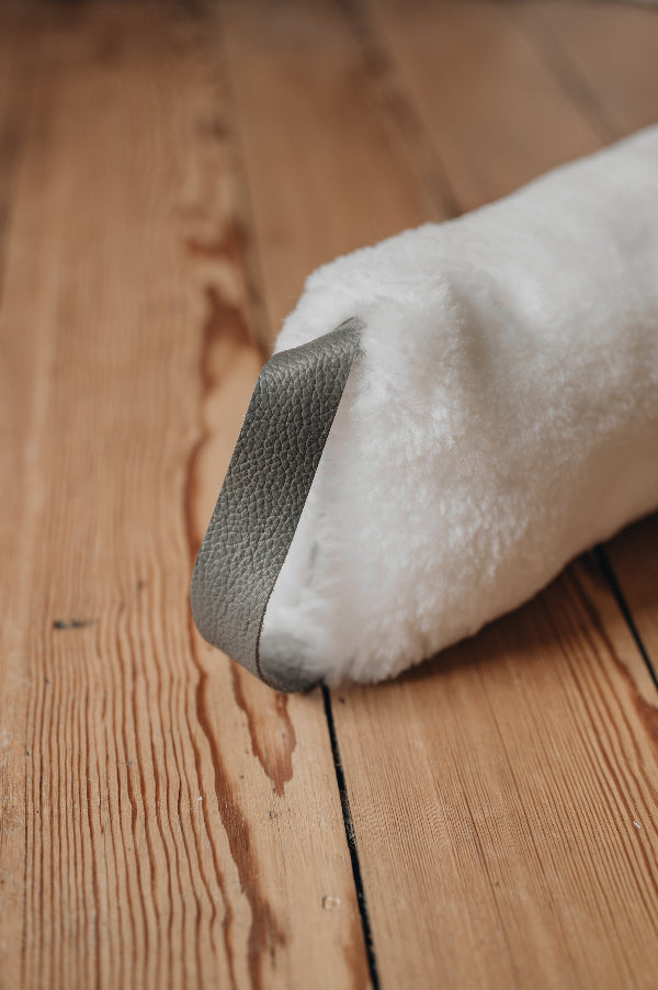 White sheepskin draught excluder with brown / grey leather hang tab on a wooden floor