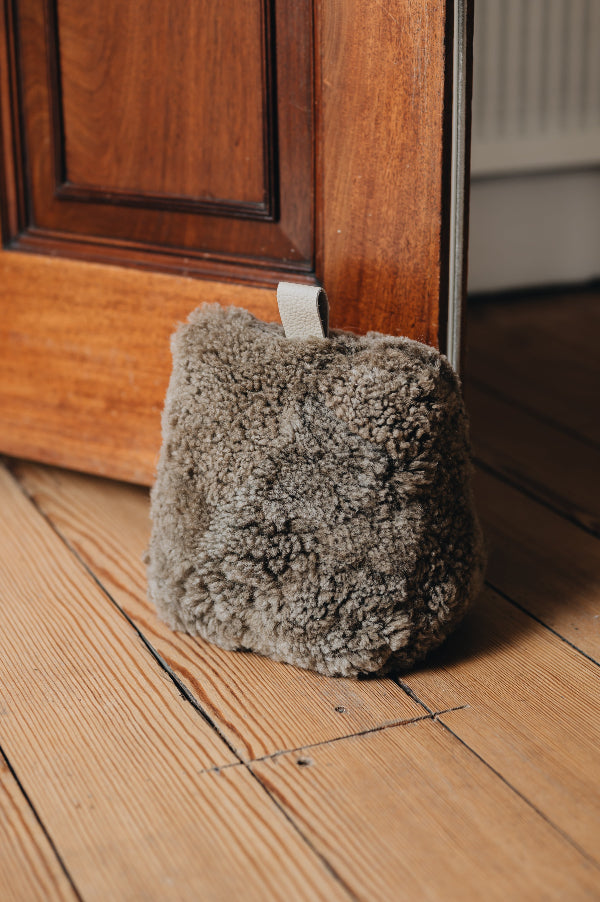 An oatmeal door stop with leather tabs, holding a wooden door open, on a wooden floor