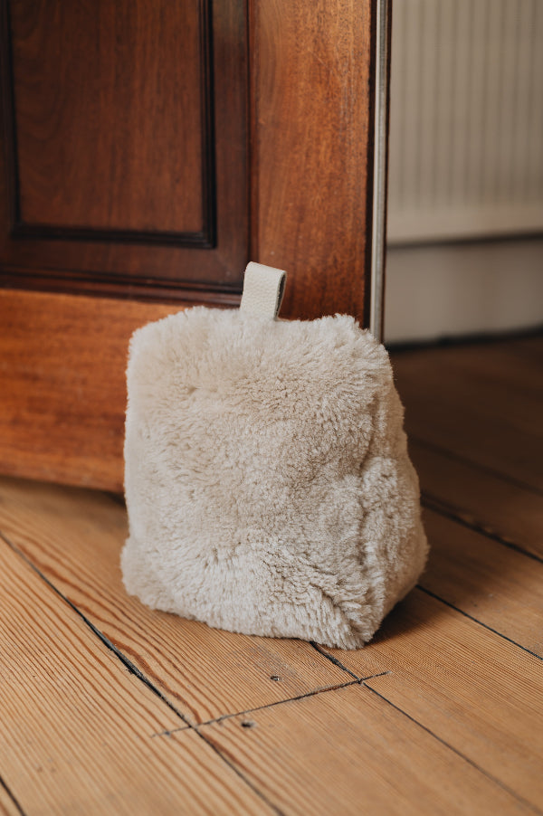 An oatmeal door stop with leather tabs, holding a wooden door open, on a wooden floor