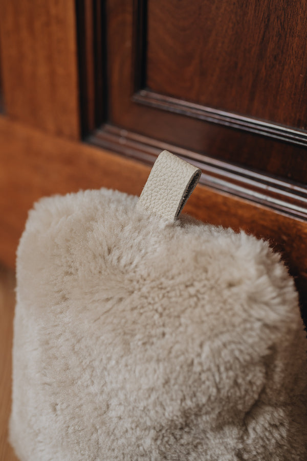 Close up of an oatmeal door stop with leather tab, holding a wooden door open, on a wooden floor