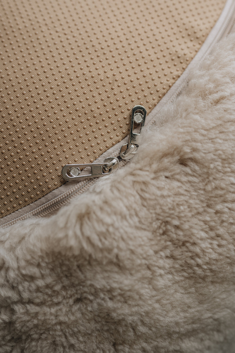 Close-up of a zipper on a beige fabric surface that is the bottom of a sheepskin beanbag.