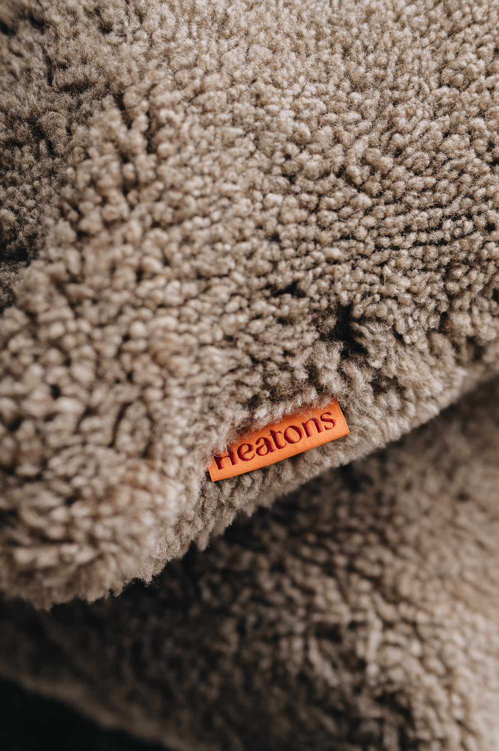 Close-up of a textured wheat brown sheepskin floor cushion with an orange  'Heaton's' label.