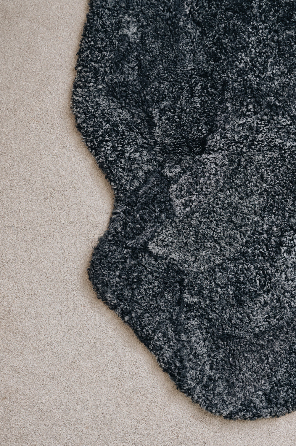 Close-up of a black smoke coloured sheepskin rug on a light coloured carpet