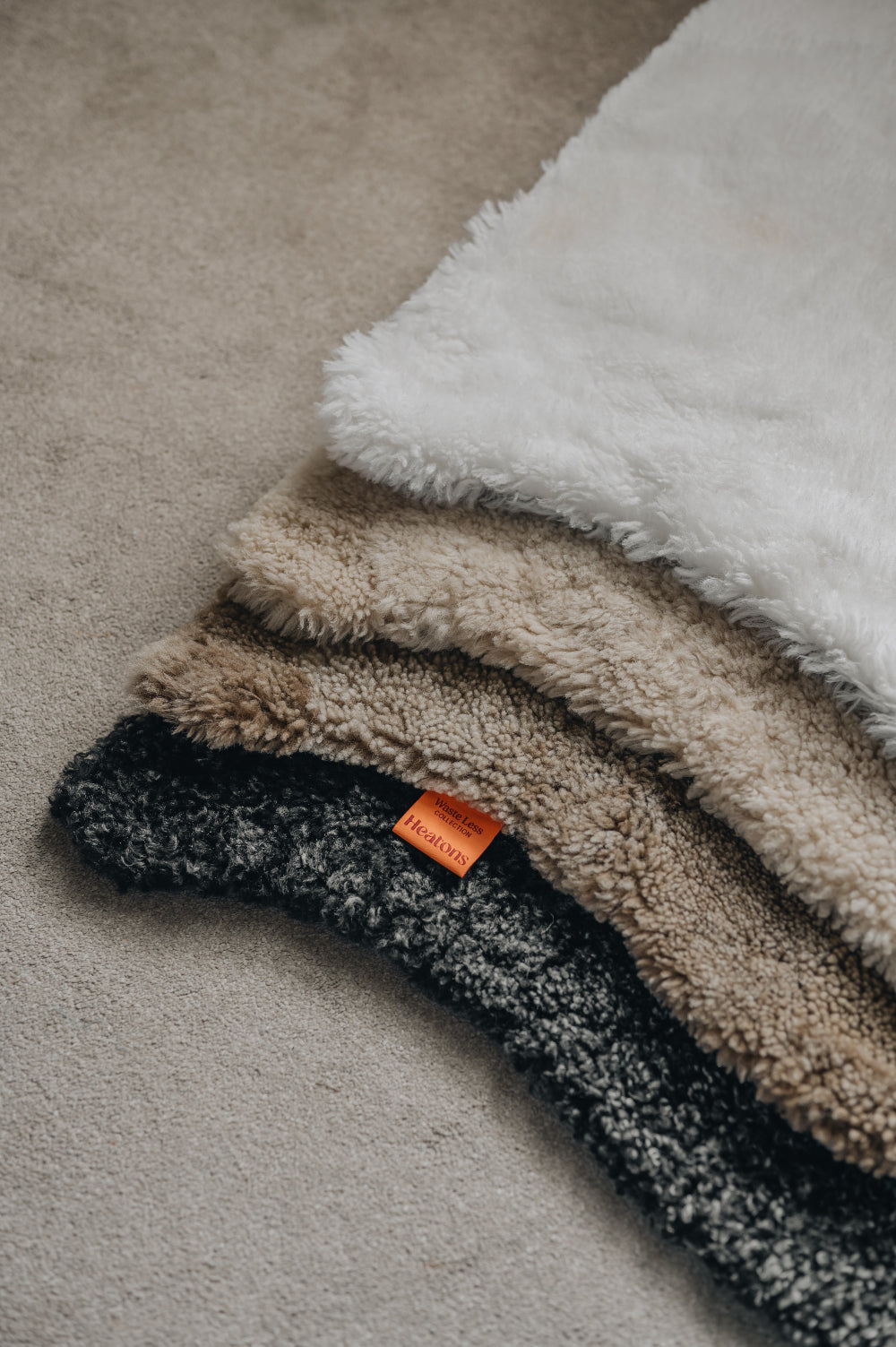 Stack of sheepskin rugs in various colours on a neutral carpet