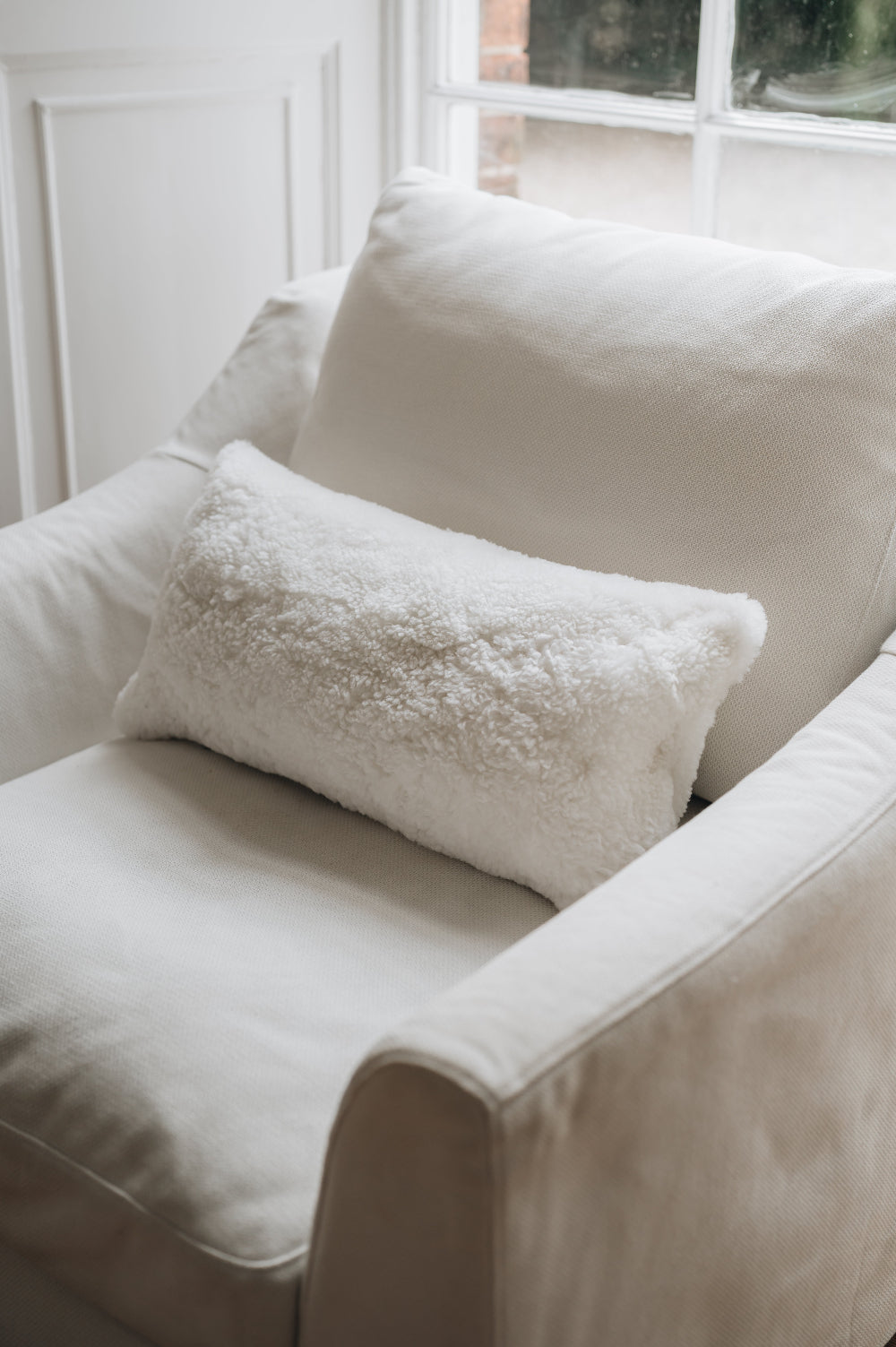 White armchair with a white sheepskin pillow in a softly lit room.