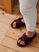 Woman in white trousers wearing Burgundy merino sheepskin slider slippers on a wooden floor