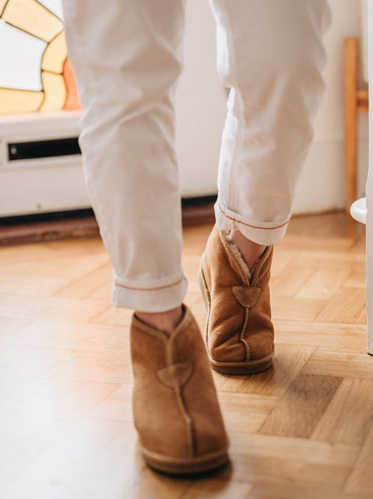 Lady in white trousers wearing Sheepskin slipper Boots with a sole walking on a wooden floor