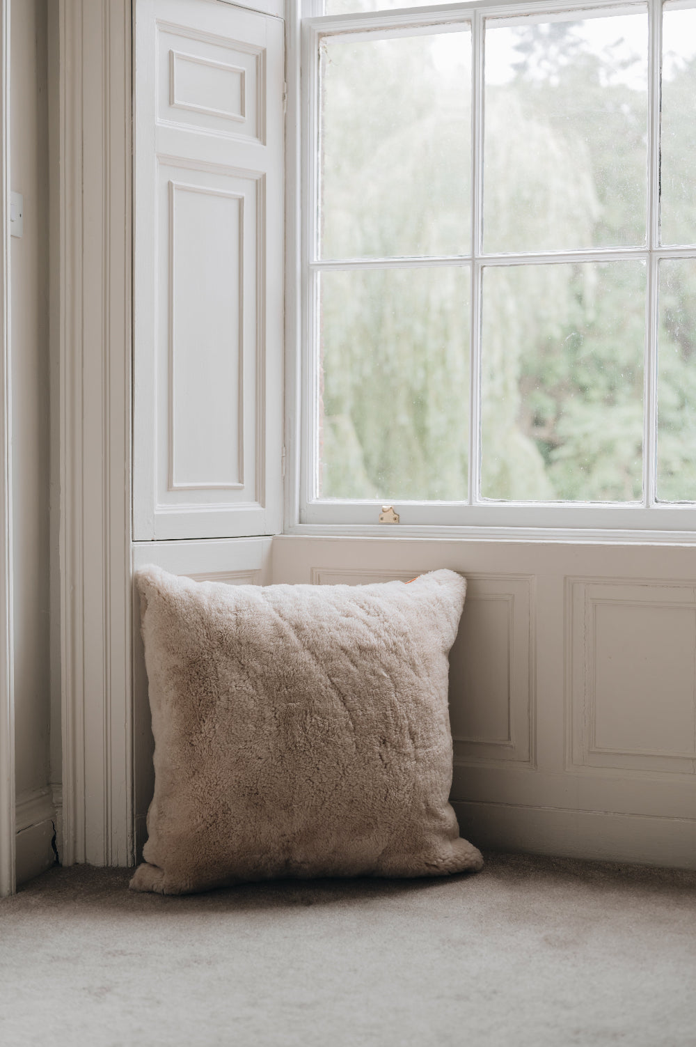 Oatmeal sheepskin floor cushion on a floor in a room with a large window