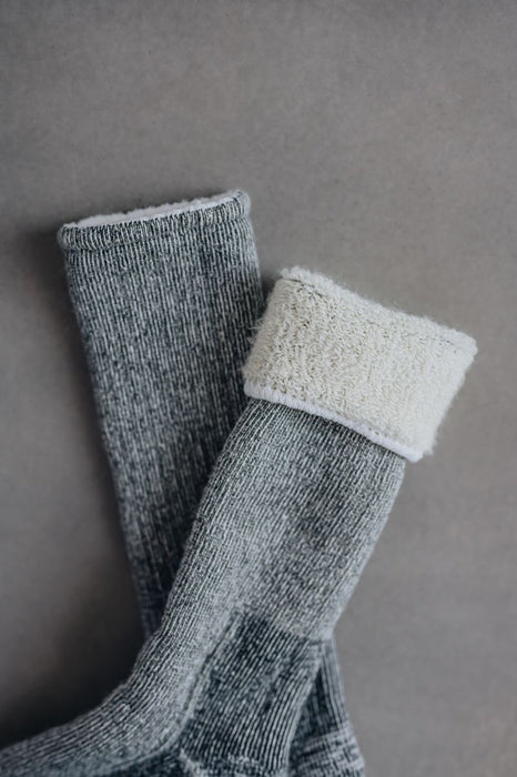 Pair of grey and black merino socks with cuff turned over showing white looped wool inner on a grey background