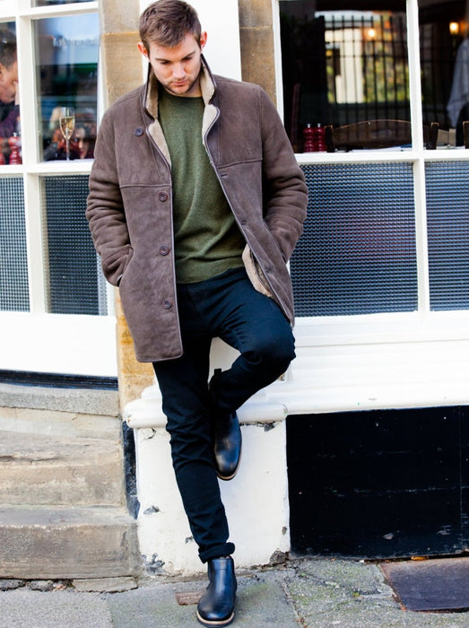 Male model wearing Men's Sheepskin brown Edward Coat, leaning against the wall of a restaurant.