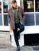 Male model wearing Men's Sheepskin brown Edward Coat, leaning against the wall of a restaurant.