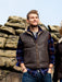 Men's Sheepskin Gilet, with collar, frotn zip and pockets. Male model stands near rocky backdrop.